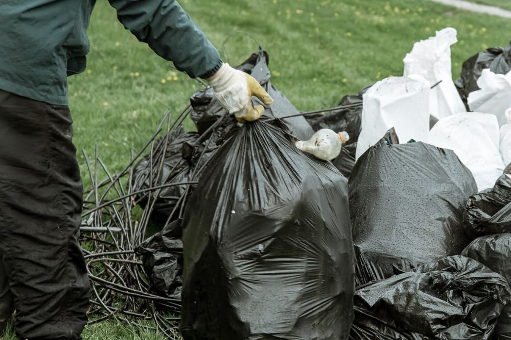 A man is seen picking up trash bags from the grass during a junk removal service in Aurora, CO.